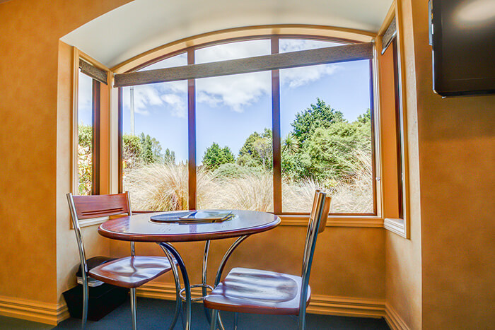 Red Tussock Motel's Superior Queen Studio dining area with table and two chairs looking out window to the tussocks 